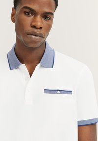 Witte polo shirt met een kraag en zakrand in blauwe strepen, met knoopsluiting en korte mouwen. Glad stoftextuur.