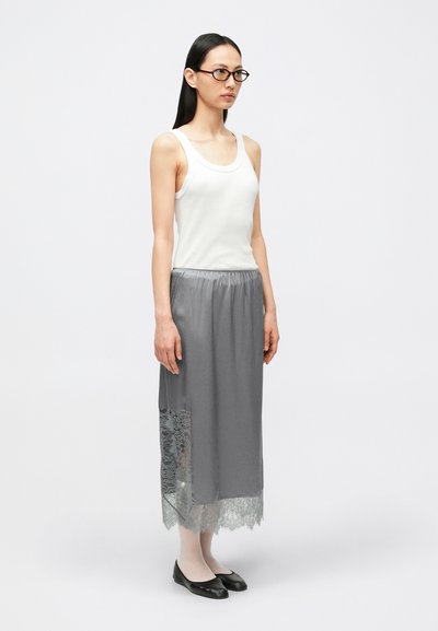 Fustă maxi gri cu talie elastică și dantelă pe o parte, combinată cu un top alb fără mâneci; pantofi negri comozi completează ținuta.