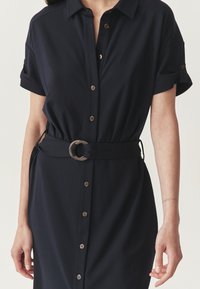 Rochie cămașă de culoare bleumarin, cu mâneci scurte, închidere cu nasturi, talie ajustată cu cataramă circulară, material neted fără modele sau texturi distincte.