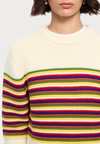 Pull en tricot épais crème avec des rayures horizontales multicolores en rouge, vert, jaune, bleu et marron ; col et poignets côtelés.
