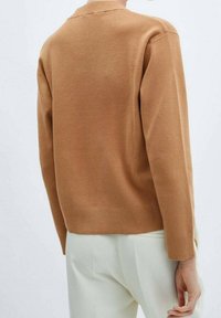 Suéter de punto color beige con cuello redondo, puños y dobladillo acanalados, y una textura suave, llevado sobre pantalones de color claro.