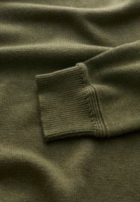 Olivgrön stickad tröja med ribbad mudd och slät textur. Tyget har en subtil lyster och intrikata sömmar.