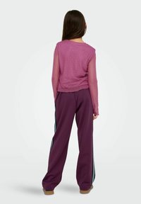Purple long-sleeve top with sheer sleeves and subtle polka dots, paired with loose-fitting purple pants featuring black and white side stripes.