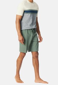 T-shirt à manches courtes bicolore en crème, gris et vert foncé, associé à un short en vert avec taille élastique. Le matériau semble doux et décontracté.