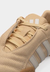 Μπεζ πάνινο παπούτσι από σουέτ με ανοιχτό γκρι ρίγες, μπεζ κορδόνια και υφασμένο καουτσούκ πάτο, που δείχνει κοντινή λήψη του μπροστινού ανώτερου μέρους.