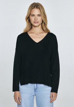 Maglietta nera a maniche lunghe con scollo a V, dal taglio comodo, realizzata in tessuto morbido. Abbinata a jeans azzurri chiari, con etichetta sull'orlo.