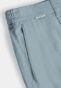 Pantalon en tissu bleu clair texturé avec ceinture élastique et poche latérale cousue, arborant une petite étiquette blanche portant l'inscription "MR MARVIS".