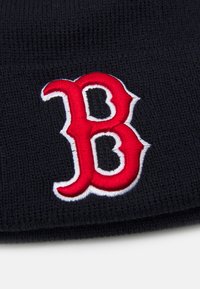 Gorro de punto negro con un destacado logo rojo bordado con una 'B' contorneada en blanco. Textura suave y ajuste ceñido.