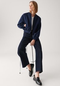 Marineblauw bomberjack, lichtgewicht stof, geribbelde manchetten, gedragen over een witte top en een donkerdenim wijde broek, gecombineerd met zwarte loafers.