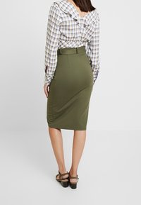 Grüne, taillierte Bleistiftrock mit Raffung, kombiniert mit einem beige-blauen Karotop mit Rüschenausschnitt und langen Ärmeln.