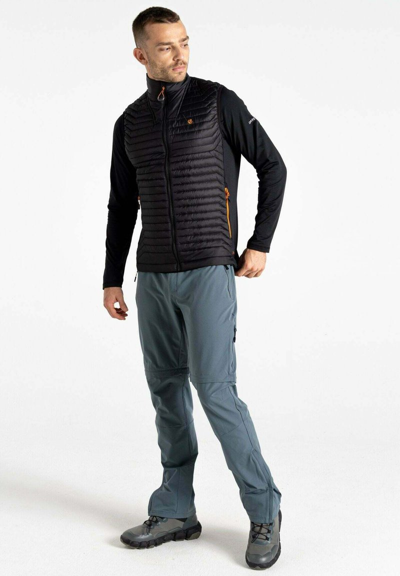 Schwarze Daunenweste mit gestepptem Design, Reißverschlusstaschen und orangefarbenen Akzenten. Kombiniert mit hellgrauen Hosen und robusten schwarzen Stiefeln.