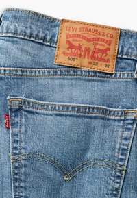 Lichtblauwe denim jeans met een leren label dat prominent "Levi Strauss & Co." en het modelnummer "505" toont. Gele stiksels accentueren het geheel.