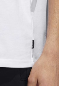 Vit bomull t-shirt med sidoflagga, korta ärmar och rak fåll. Tyget ser slätt och lätt ut.