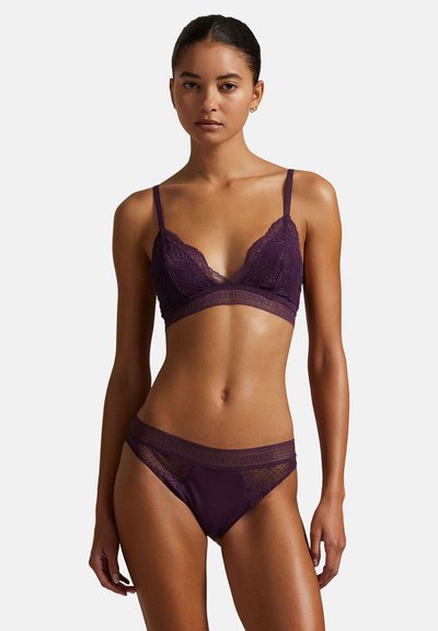 Pitkä pitsiliivikupit ja siihen sopivat stringit syvän violetissa, joissa on herkkää pitsireunusta, säädettävät olkaimet ja logolla varustettu vyötärönauha. Sileä pintamateriaali.