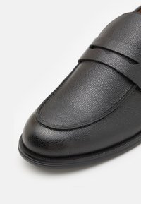 Gros plan d'une chaussure habillée en cuir noir avec une finition texturée et un design classique à bride penny loafer.