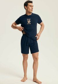 Granatowa koszulka z napisem "CIESZ SIĘ PRZYRODĄ" i grafiką liścia, zestawiona z granatowymi szortami, wykonana z miękkiego materiału, luźny krój, minimalistyczny design.