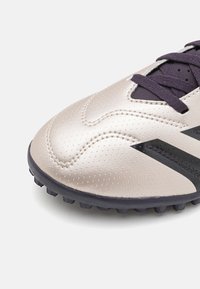 Scarpa da calcio con tomaia metallica argento, superficie testurizzata, dettagli neri e lacci viola scuro. Suola in gomma con tacchetti per trazione.