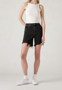 Pantalones cortos de mezclilla negros con dobladillo deshilachado, diseño de talle alto y dos bolsillos delanteros. Combinados con una camiseta entallada de canalé blanca y zapatillas blancas.