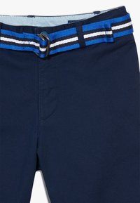 Námořnické modré šortky s tkaným pásem s modrými, bílými a černými pruhy, kovovou sponou a plochým předním designem. Hladká textura látky.