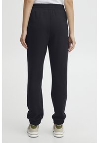 Sorte joggebukser med elastisk midje og mansjetterte ankler, laget av et mykt materiale, kombinert med lyse sneakers.