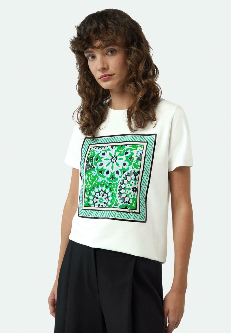 Witte katoen t-shirt met een kleurrijke bloemenprint in groen, blauw en zwart, omlijst door een geometrische zwarte rand en een geruit accent.