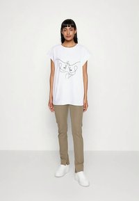 Valge lühikeste varrukatega T-särk, millel on kahe näo must joonistus. Sobitatud beežide pükste ja valgete tossudega.