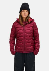 Red puffer jacket with wave pattern, zipper closure, and hood. Worn over a matching top, paired with dark pants and a black knit beanie.