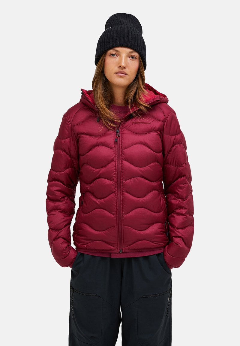 Red puffer jacket with wave pattern, zipper closure, and hood. Worn over a matching top, paired with dark pants and a black knit beanie.