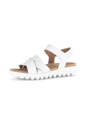 White sandal with crisscross straps, adjustable ankle strap, cushioned tan footbed, and thick white ridged sole.