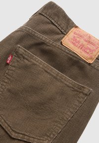 Gros plan sur un pantalon Levi's en velours côtelé marron montrant la poche arrière, l'étiquette rouge Levi's et le patch de marque en cuir beige sur la ceinture.