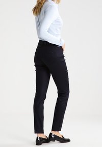 Navy blue tailored pants with a straight leg fit, featuring side pockets and a smooth cotton blend material. Worn with a light blue top.