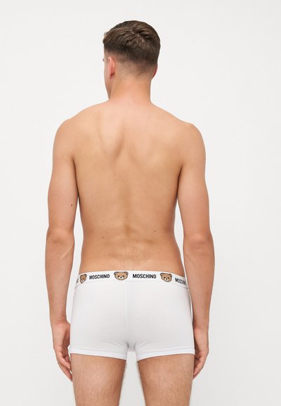Weiße Baumwoll-Boxershorts mit einem schwarzen Bund, der ein Bärenlogo und den Schriftzug "MOSCHINO" zeigt. Sie bieten eine enge Passform und eine glatte Textur.