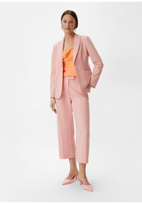 Różowa marynarka z klapami oraz różowe, krótkie spodnie. Pod spodem pomarańczowa satynowa bluzka. Całość dopełniają różowe, spiczaste szpilki.