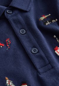 Marineblauw poloshirt met drie zwarte knopen, voorzien van geborduurde vakantie-motieven, waaronder auto's, bomen en geschenken op een textiel met structuur.