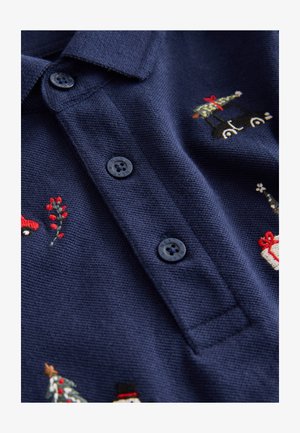 Camiseta polo azul marino con tres botones negros, con motivos navideños bordados, incluyendo coches, árboles y regalos sobre una tela texturizada.