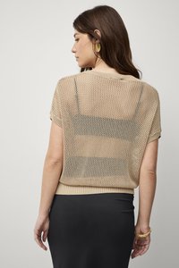 Nude-kleurige gebreide top met een losse, mesh-ontwerp, korte mouwen en geribbelde zoom, gecombineerd met een zwarte rok.
