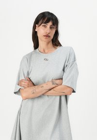 Light grey oversized t-shirt made of soft fabric, featuring a round neck and a small metallic logo detail near the neckline.
