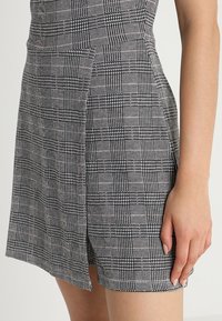 Pantalones cortos de patrón en blanco y negro con un diseño a cuadros. El material parece suave; cuenta con una abertura lateral y un ajuste estilizado.