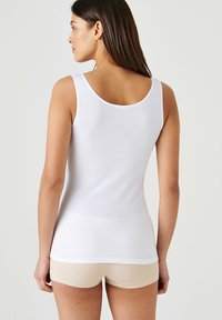 Top bianco senza maniche con scollatura rotonda, forma aderente e texture liscia, abbinato a pantaloni corti beige.