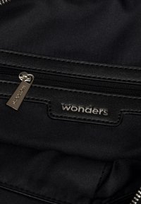 Czarny plecak z materiału z zamykaną na zamek kieszenią i srebrnym uchwytem. Słowo "wonders" jest wytłoczone w metalicznym tekście na skórzanej łatce.