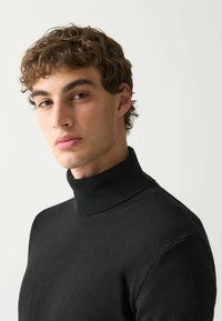 Črna pulover turtleneck iz mehke tkanine. Ima prilegajoč dizajn in rebrast ovratnik, ki zagotavlja toploto in poenostavljeno silhueto.