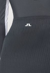 Veste atlética preta com textura em relevo, apresentando um logótipo branco na cintura. Projetada com mangas longas e uma silhueta elegante e ajustada.