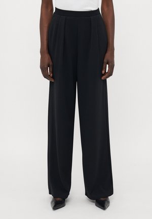 Black wide-leg trousers with pleats, smooth texture, high waistband, and front crease, paired with pointed black shoes.