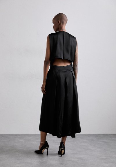 Black sleeveless top with a cropped design, paired with a flowing black skirt. Material appears smooth and soft, with a subtle sheen.