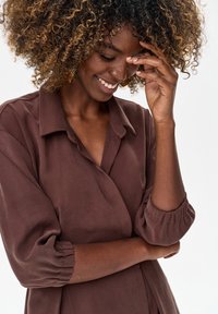 Brązowa koszula z długim rękawem o luźnym kroju, z kołnierzykiem i marszczonymi rękawami, wykonana z miękkiego materiału o gładkiej teksturze.