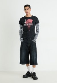 Camiseta gráfica negra con el texto "Me encanta el RECHAZO", mangas largas con patrón de cebra, culottes de mezclilla oscuros y zapatos de plataforma negros con tachuelas.