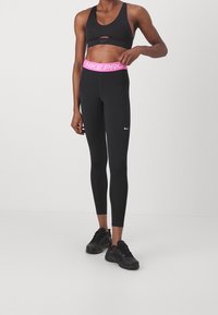 Black athletic leggings with pink "NIKE PRO" waistband, fitted design, paired with a black sports bra featuring a front cutout detail.