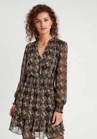 Robe à motif noir et marron avec une taille smockée, des manches longues et un ourlet volé. Présente des motifs floraux et géométriques en tissu transparent.