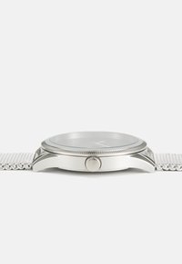 Silbernes Mesh-Armbanduhren mit einem runden Gehäuse, glattem Glas, strukturiertem Bezel und einer mittigen Krone. Minimalistisches Zifferblatt mit dezenten Stundenmarkierungen.