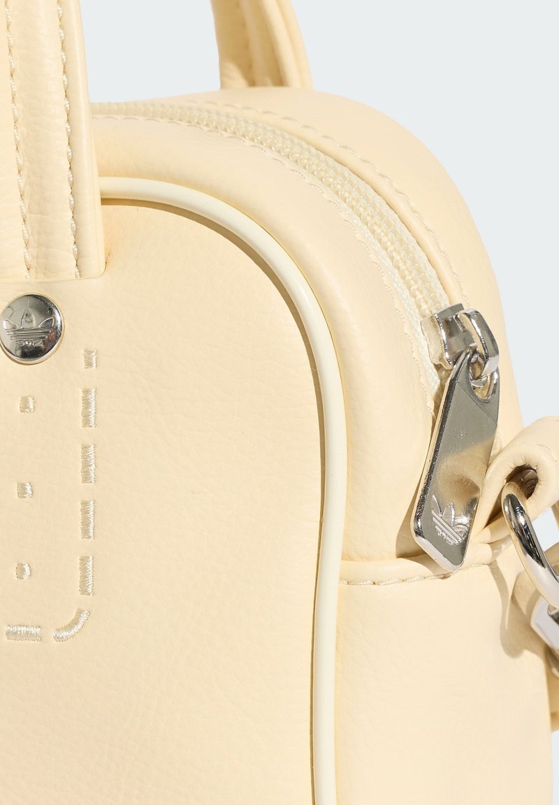 Borsa in pelle color crema con cursore della cerniera argentato e rivetto metallico, con dettagli cuciti e un corto manico a loop.
